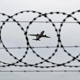 Ein Flugzeug startet, fotografiert durch Stacheldraht am Flughafenzaun.