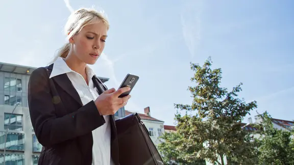 Eine junge Frau mit einer Aktentasche schaut auf ihr Smartphone (gestellte Szene).