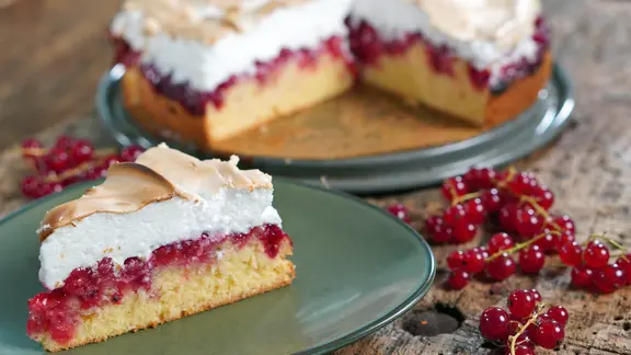 Johannisbeerkuchen mit Baiser steht angeschnitten auf einem Teller