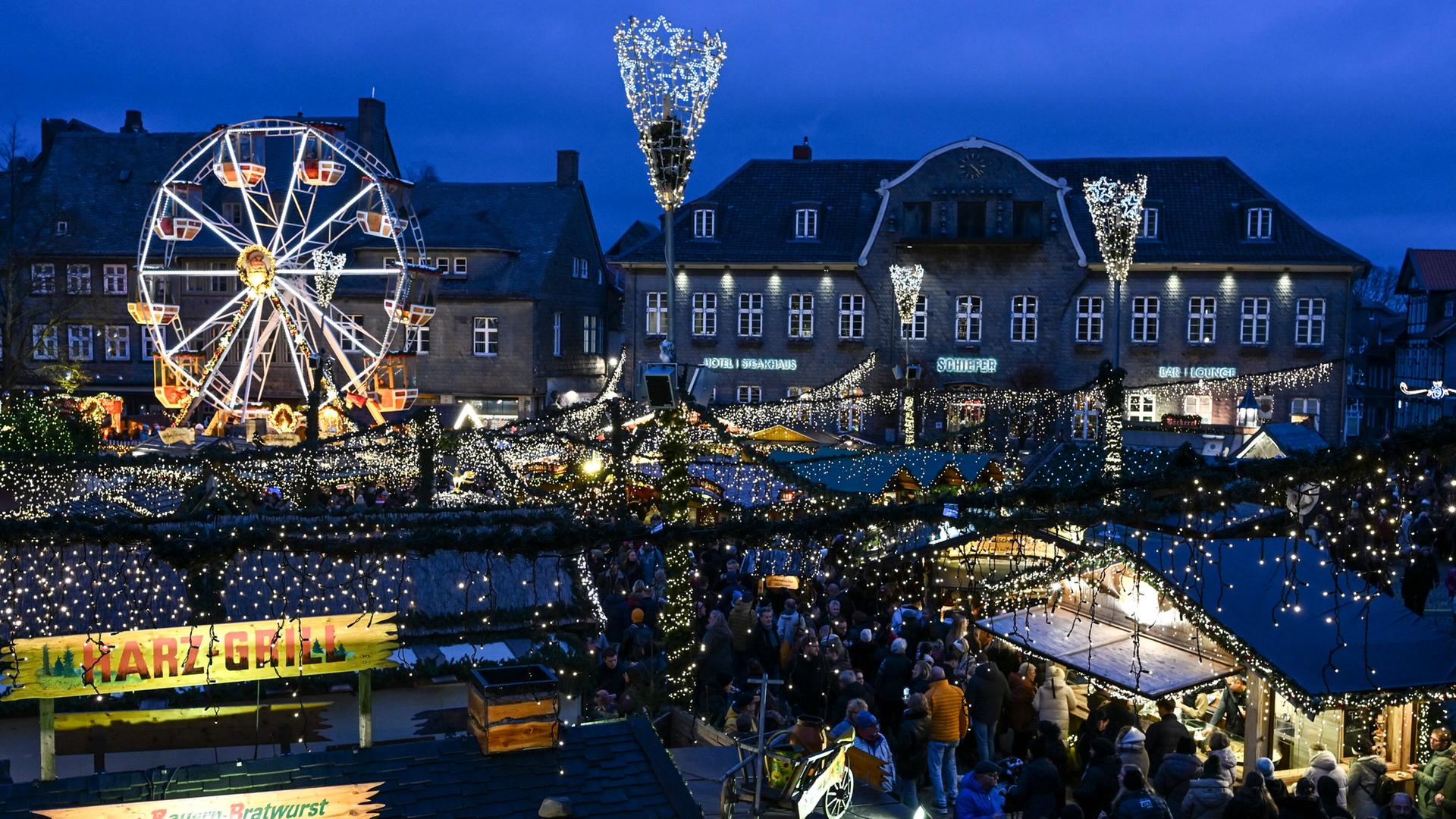 Viele Menschen besuchen abends einen Weihnachtsmarkt auf dem ein kleines Riesenrad steht. | picture alliance/dpa | Jens Kalaene