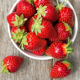 Blick von oben auf eine Schale mit Erdbeeren auf einem Holztisch.