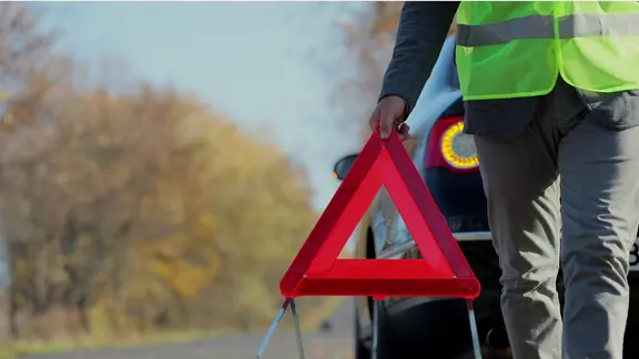 Ein Mann mit Warnweste hält ein Warndreieck in der Hand.