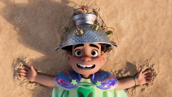 Szene aus dem Kinofilm "Elio": Ein kleiner Junge in seltsamer Verkleidung liegt im Sand