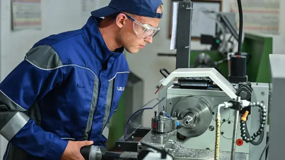 Ein Auszubildender zum Mechatroniker arbeitet an einer Drehmaschine.