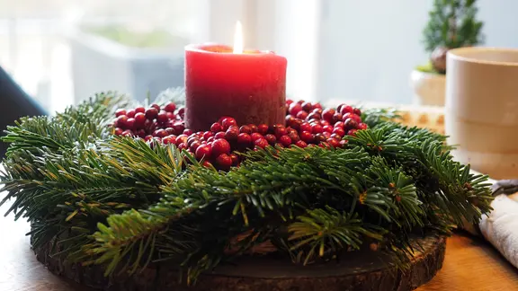 Eine schlichte rote Stumpenkerze in einem Adventskranz aus Tannengrün mit roten Beeren dekoriert. | NDR, Anja Deuble Eine schlichte rote Stumpenkerze in einem Adventskranz aus Tannengrün mit roten Beeren dekoriert.