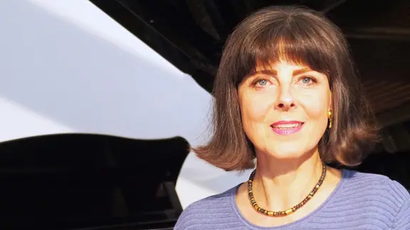 Eine Frau mit schulterlangen Haaren und lila Pulli lächelt in die Kamera