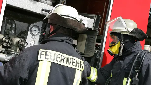 Zwei Feuerwehrleute an einem Einsatzfahrzeug.