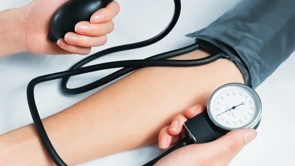 Eine Frau misst den Blutdruck am Oberarm eines Patienten.
