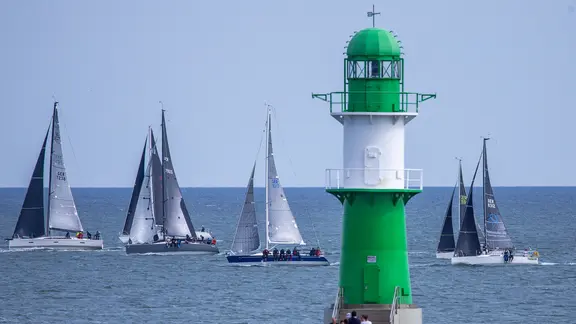 Segelschiffe fahren auf der Ostsee vor Warnemünde hinter dem grünen Molenfeuer vorbei. (Themenbild)