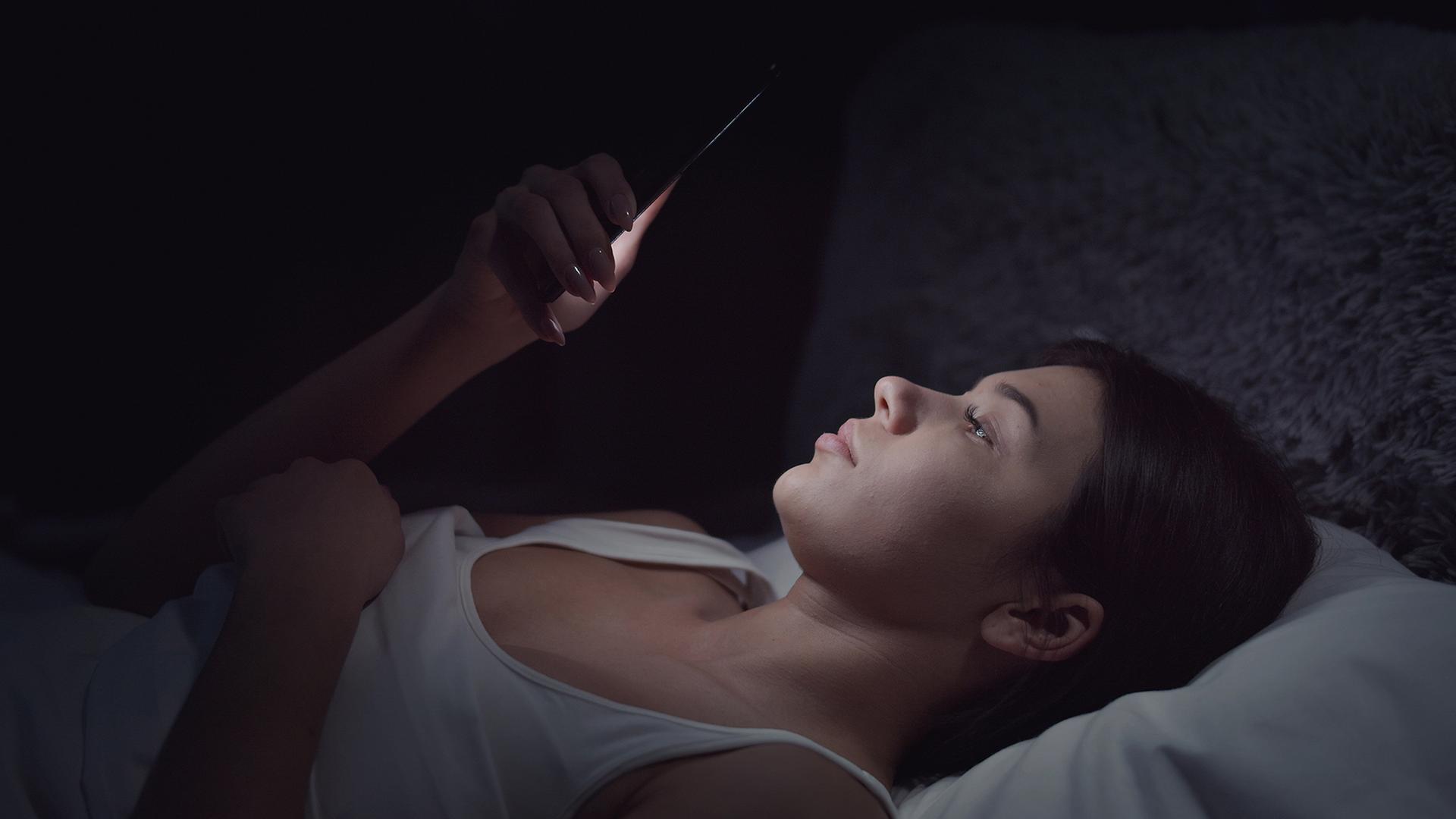 Eine junge Frau liegt im Bett und schaut auf ein Smartphone | Colourbox/Vitaliy Nykolyshyn