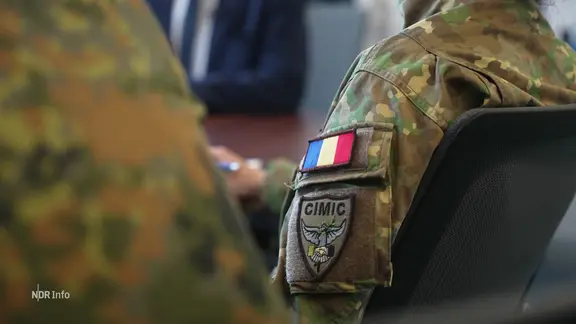 Eine sitzende Person trägt eine Militäruniform in Tarnfarben mit einem rumänischen Flaggen-Abzeichen.
