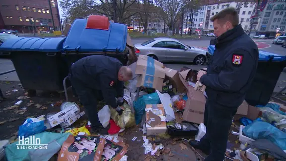 Zwei uniformierte Männer kontrollieren einen verschmutzten Müllplatz.