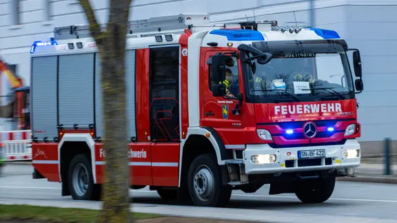Ein Feuerwehrfahrzeug fährt mit Blaulicht zum Schweriner Schloss.