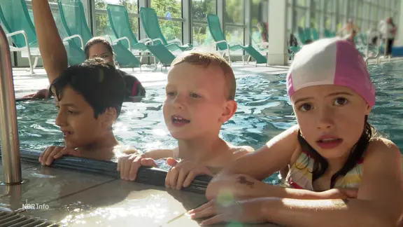 Kinder am Beckenrand eines Schwimmbades.