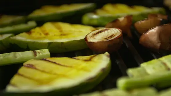 Melonenstücke, Gurken und Zwiebeln liegen auf einem Grill.
