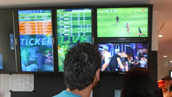 Menschen in einer Wettannahmestelle schauen auf die Monitore.