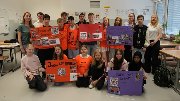 Schülerinnen und Schüler tragen selbst gestaltete T-Shirts und halten Plakate hoch.