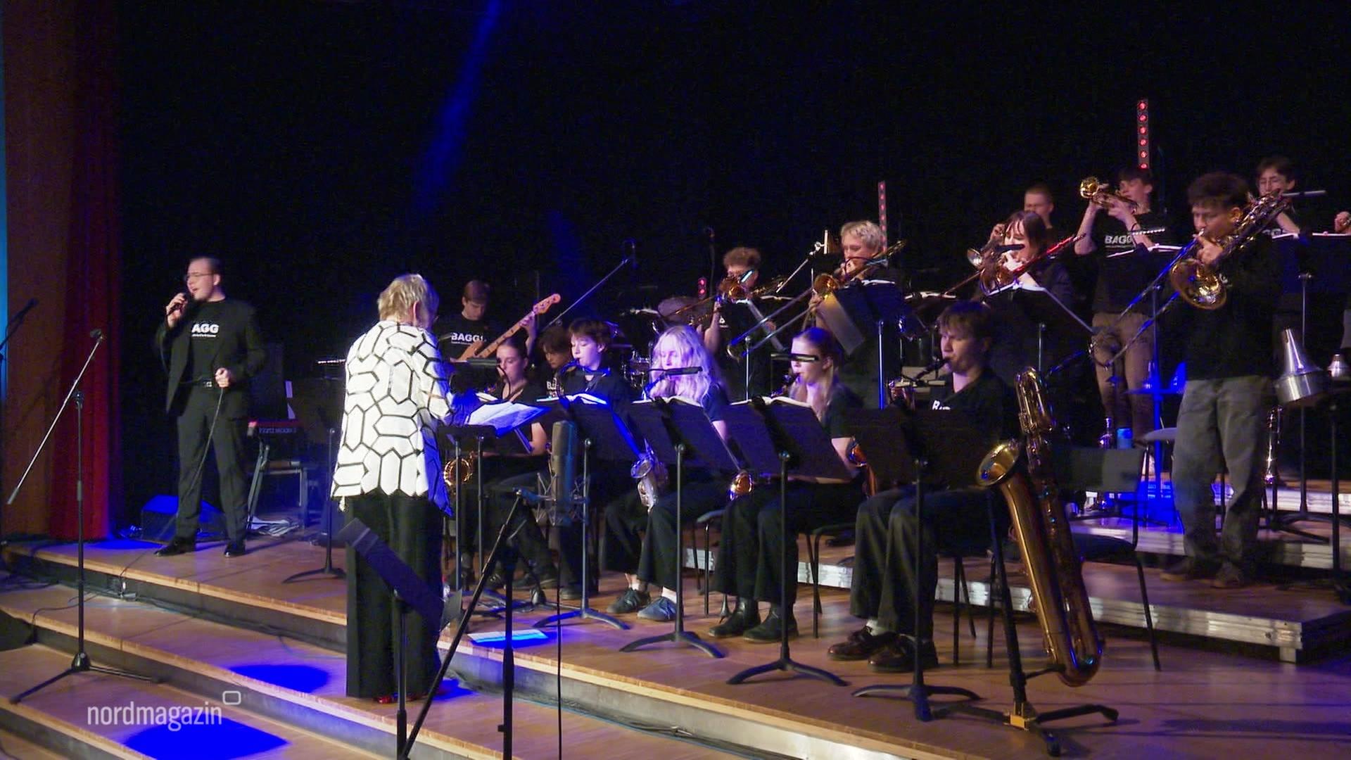 Schülerinnen und Schüler spielen in einer Bigband, vorne steht die Dirigentin. | Screenshot