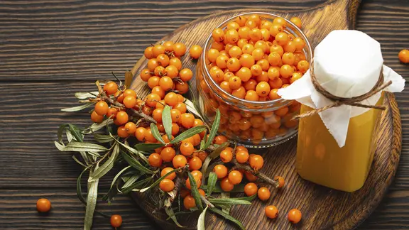 Sanddornbeeren und ein Glas mit eingekochtem Sanddorn auf einem Tisch