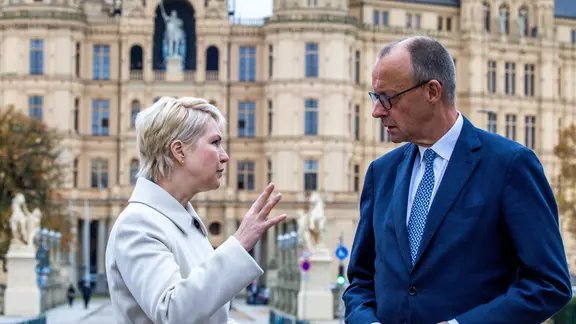 Manuela Schwesig und Friedrich Merz sprechen miteinander. Im Hintergrund: das Schweriner Schloss
