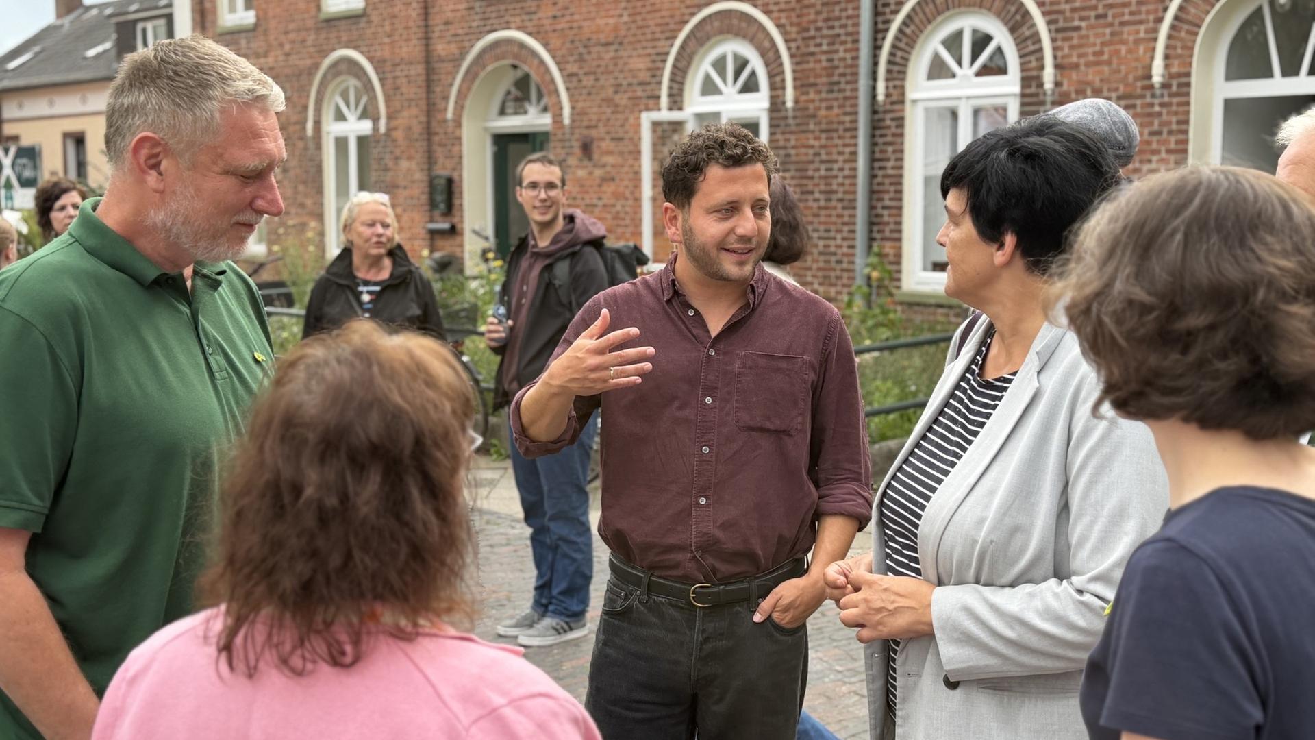 Felix Banaszak steht vor einem Gebäude und unterhält sich mit Bürgern. | NDR / Pascal Klug