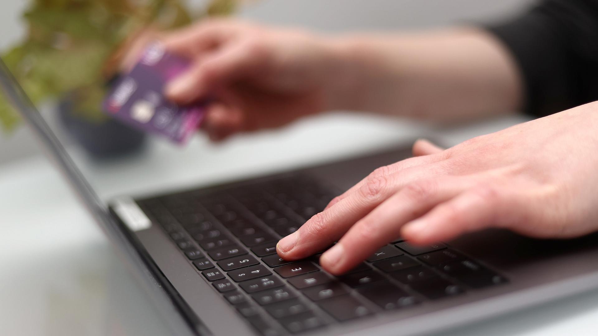Eine Person tippt auf einer Computertastatur und hält eine Bankkarte in der anderen Hand. | picture alliance / empics, Tim Goode