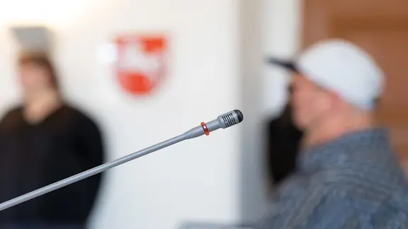 Vor einem Angeklagten in einem Bezirksgerichtssaal ist ein Tischmikrofon zu sehen.