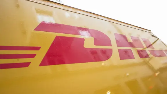 Ein Fahrzeug des Paketdienst des Lieferanten DHL. Logo im Fokus.