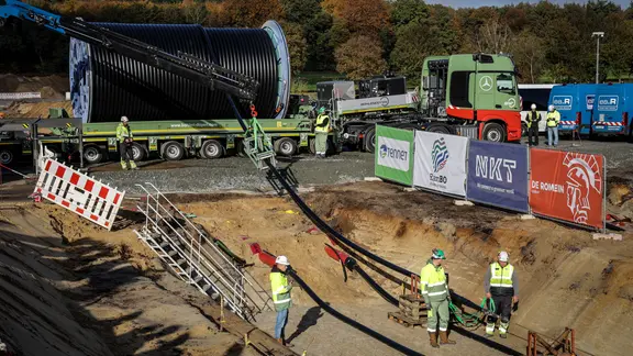 Arbeiter ziehen auf einer Baustelle der SuedLink-Trasse ein Kabel in einen Graben ein.