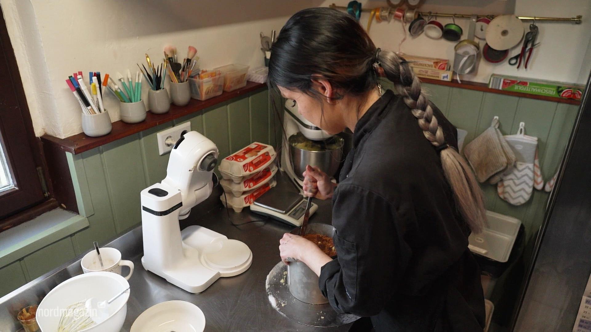 Theresa Kohl steht in der Küche und schneidet einen Kuchen aus der Form. | Screenshot