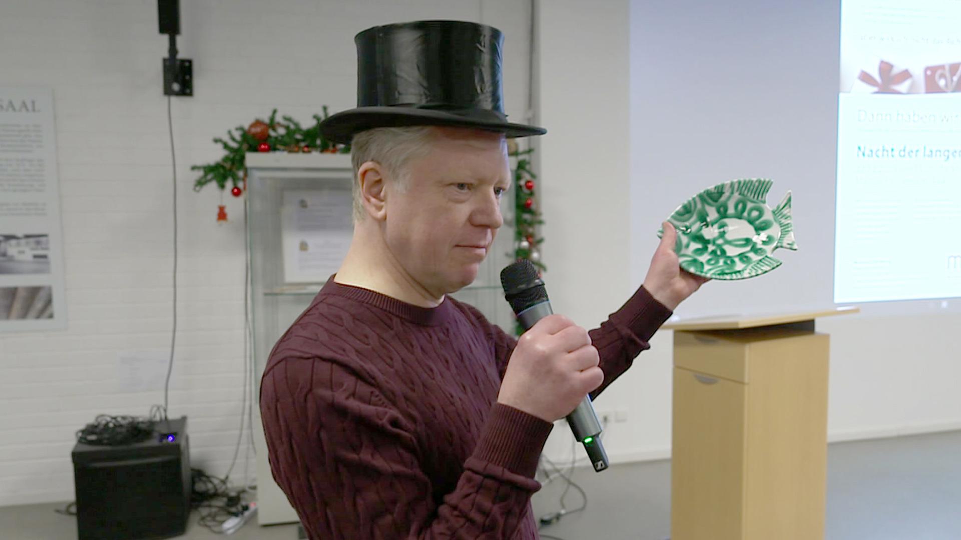 Ein Mann mit Zylinder hält einen Teller hoch. | NDR