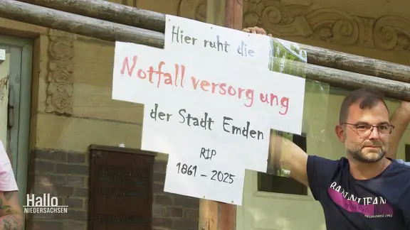 Ein Mann mit einem Plakat: "Hier ruht die Notfallversorgung der Stadt Emden".