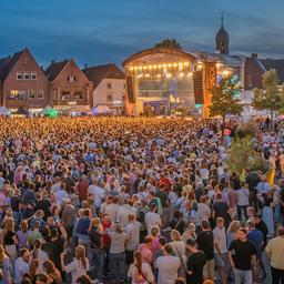 Eine Menschenmenge steht vor einer Bühne auf dem Marktplatz in Lingen. Es ist Abend.