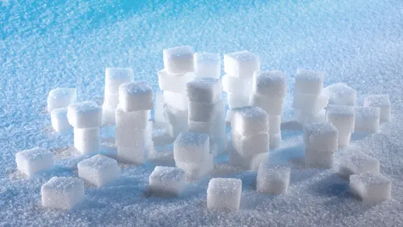 Locker gestapelte Würfelzuckerstücke auf einer Fläche mit Streuzucker.